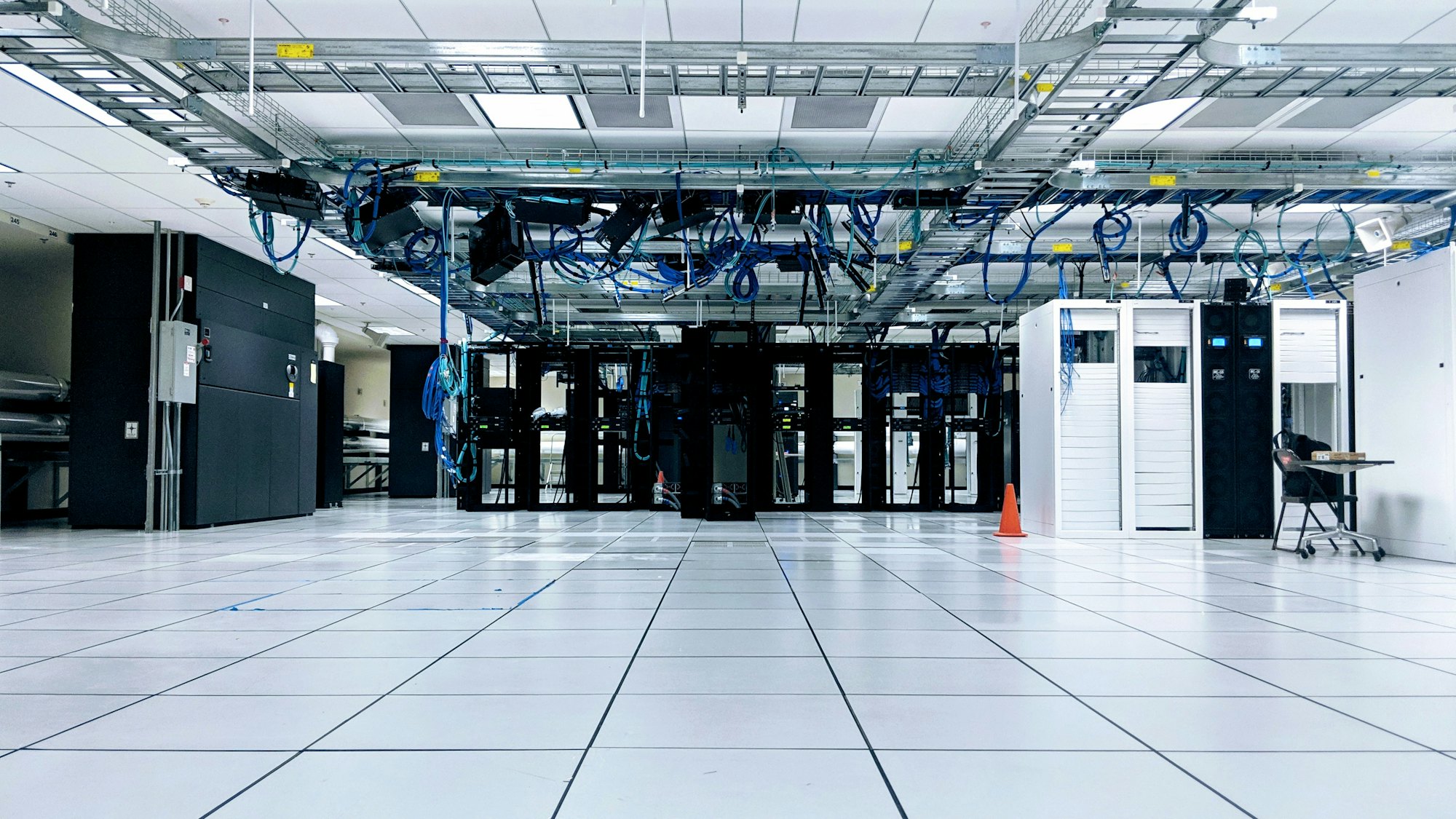 Rows of server cabinets beneath overhead cabling in a data centre